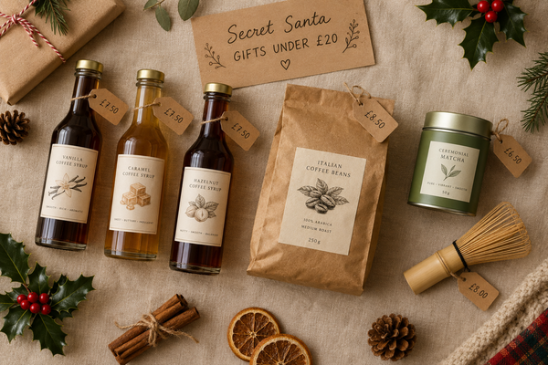 flat lay of the syrup trio, a 250 g bag of Italian Gourmet, matcha tin and bamboo whisk, all with price tags. Alt: "Secret Santa coffee gifts under £20: Sweetbird syrup trio, Coffee King Italian Gourmet beans, matcha and whisk