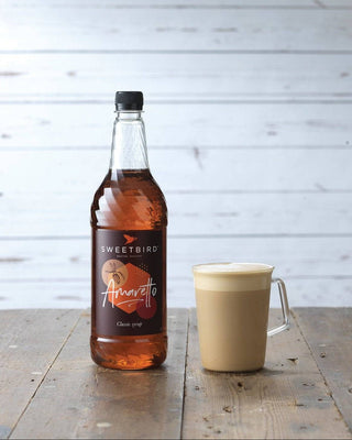 Bottle of Sweetbird Amaretto syrup next to an amaretto latte.