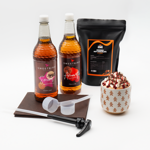 Hot chocolate setup with Sweetbird syrup bottles, a bag of hot chocolate mix, and a mug of hot chocolate.