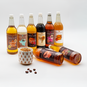 Assorted bottles of Sweetbird syrups on a white background with a small cup and coffee beans.