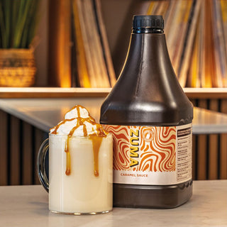 Bottle of caramel sauce with a cup of coffee and caramel drizzle on a wooden surface.
