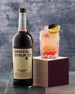 Bottle of Bristol Syrup Co. No.28 Blackberry Shrub in a 750ml glass bottle, and Blackberry Lemonade in glass
