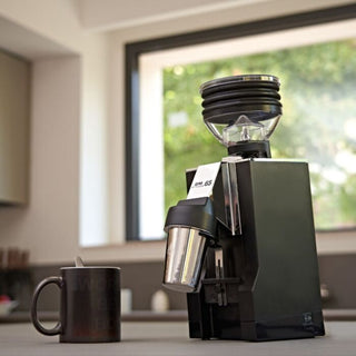 Eureka Mignon Zero AP 65 coffee grinder in black on a kitchen counter beside a coffee mug.