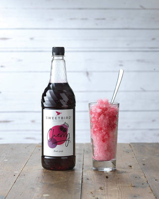 Bottle of Sweetbird Cherry Syrup with a glass of cherry cooler.
